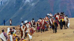 People in traditional dress walking with horses along a mountain trail.