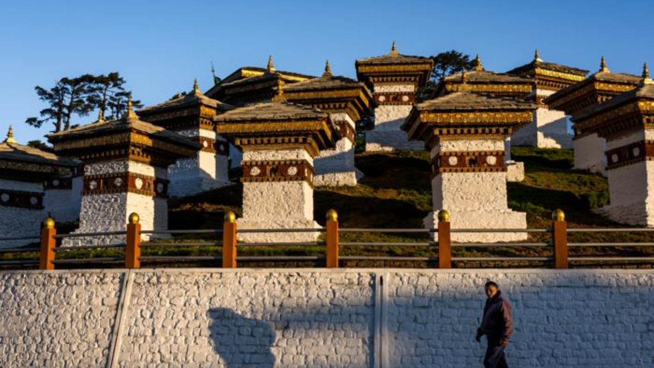 Traditional Bhutanese chortens at Dochula Pass with mountain views and a person walking along the pathway in Bhutan