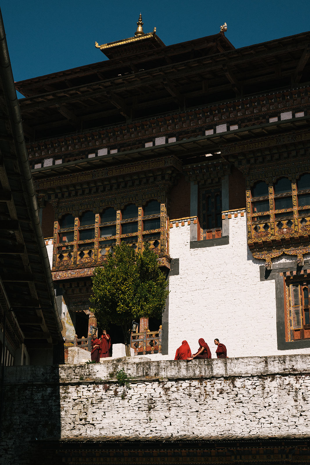 Monks in red robes walk along a stone wall outside an ornate traditional temple building