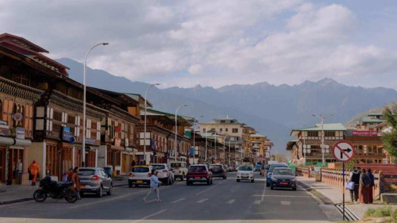 Daily life in Thimphu with cars, pedestrians, and Bhutanese-style buildings along a main road.