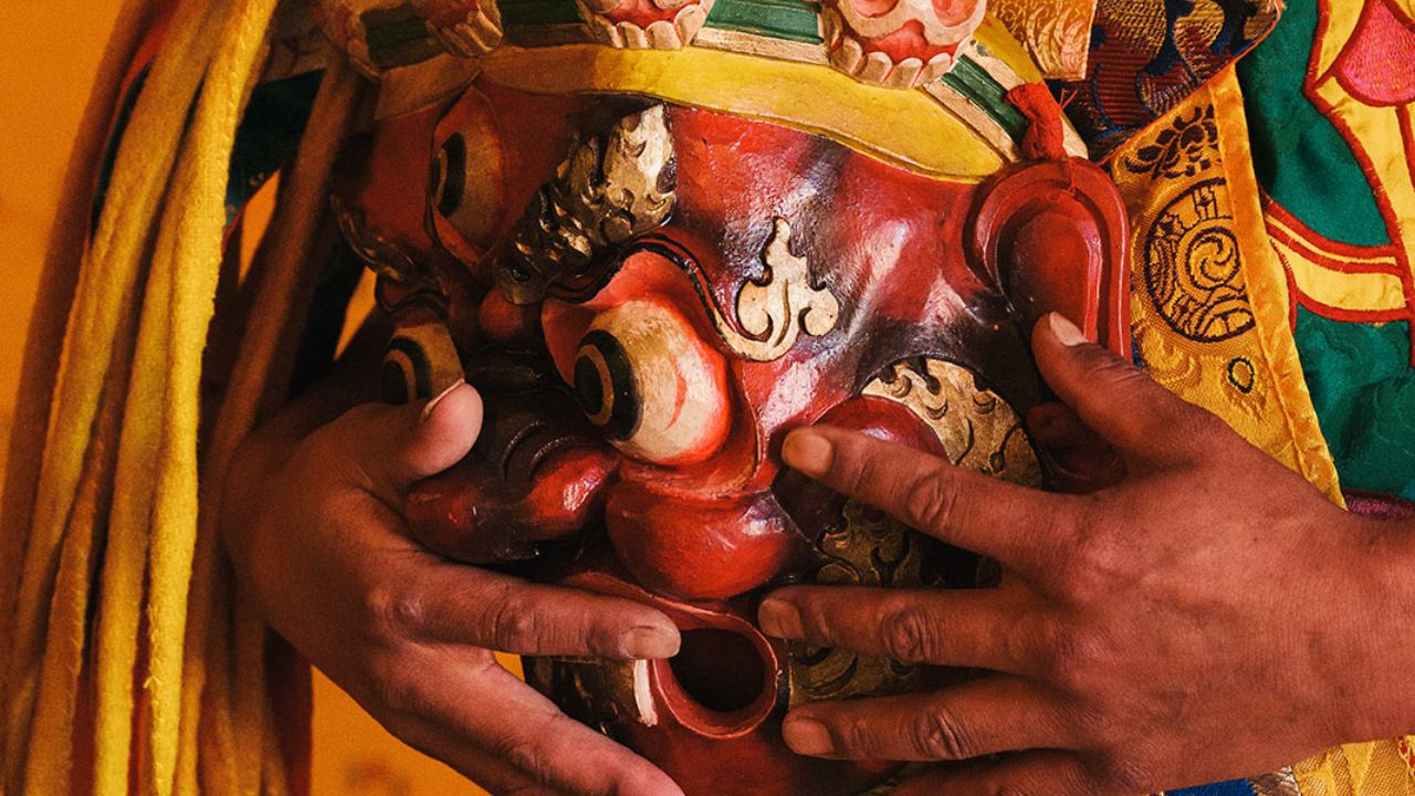 Close-up of a Bhutanese ceremonial mask with skull decorations held by a performer in traditional attire.