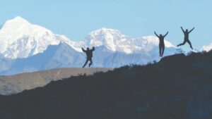 Three trekkers jumping on a ridge with snow-capped mountains in the background during the Jomolhari Trek in Bhutan.