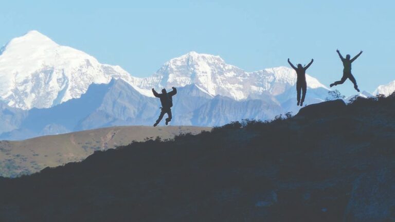 Three trekkers jumping on a ridge with snow-capped mountains in the background during the Jomolhari Trek in Bhutan.