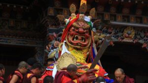Monks carrying a large masked deity statue during a traditional Bhutanese festival ceremony.