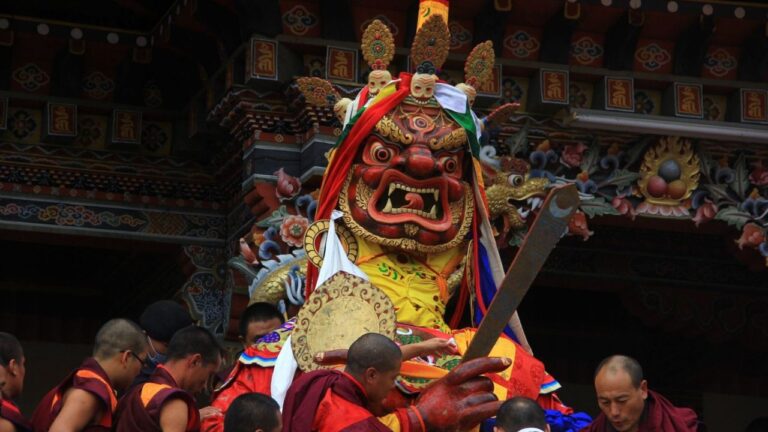 Monks carrying a large masked deity statue during a traditional Bhutanese festival ceremony.